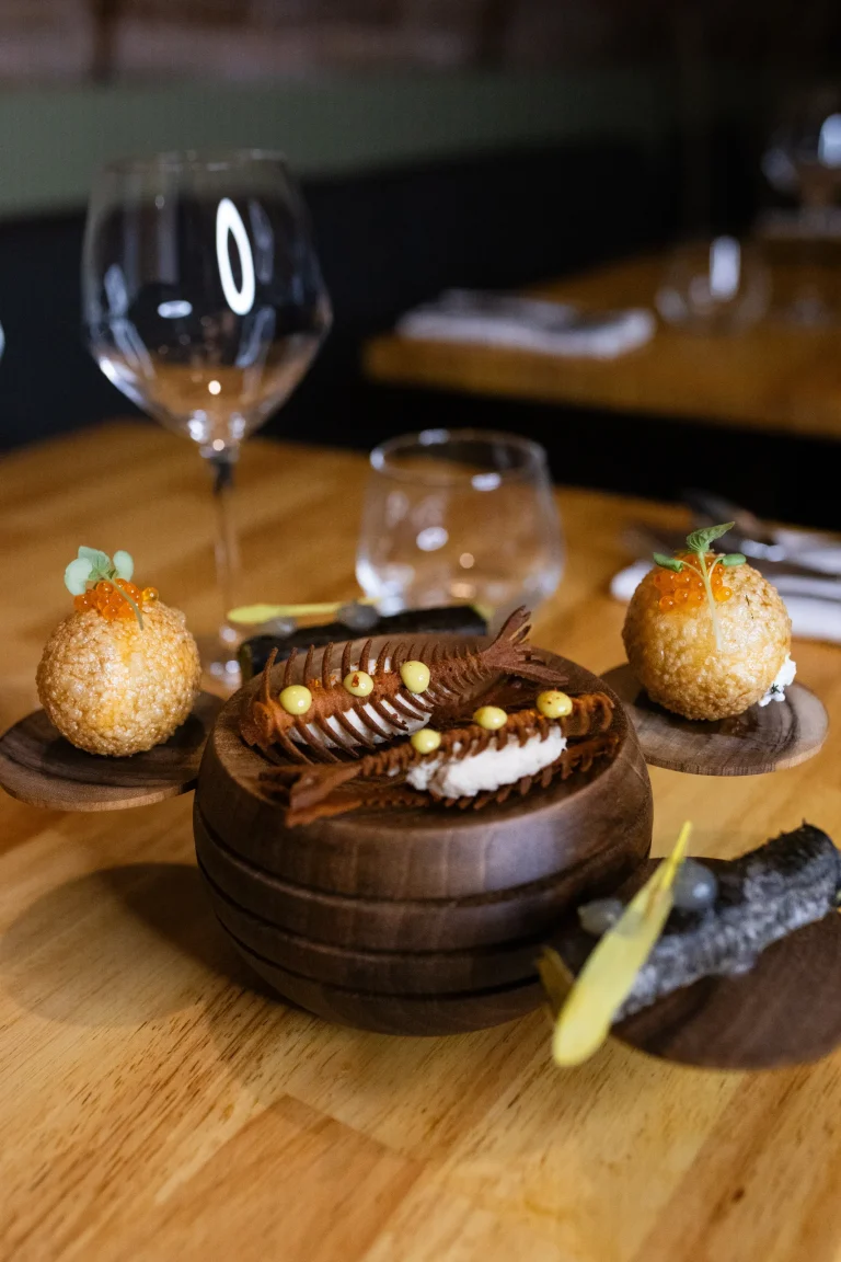 Bouchées dressées sur un présentoir en bois, verres à vin en arrière-plan
