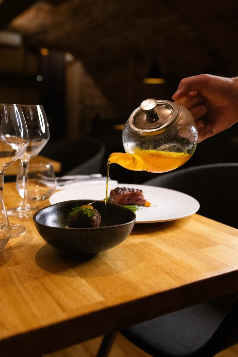 Bouillon versé à table depuis une théière en verre dans un bol noir
