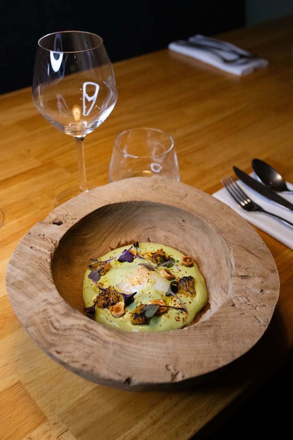 Velouté vert garni de fleurs comestibles dans une assiette creuse en bois