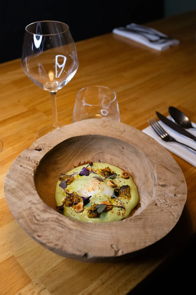 Velouté vert garni de fleurs comestibles dans une assiette creuse en bois