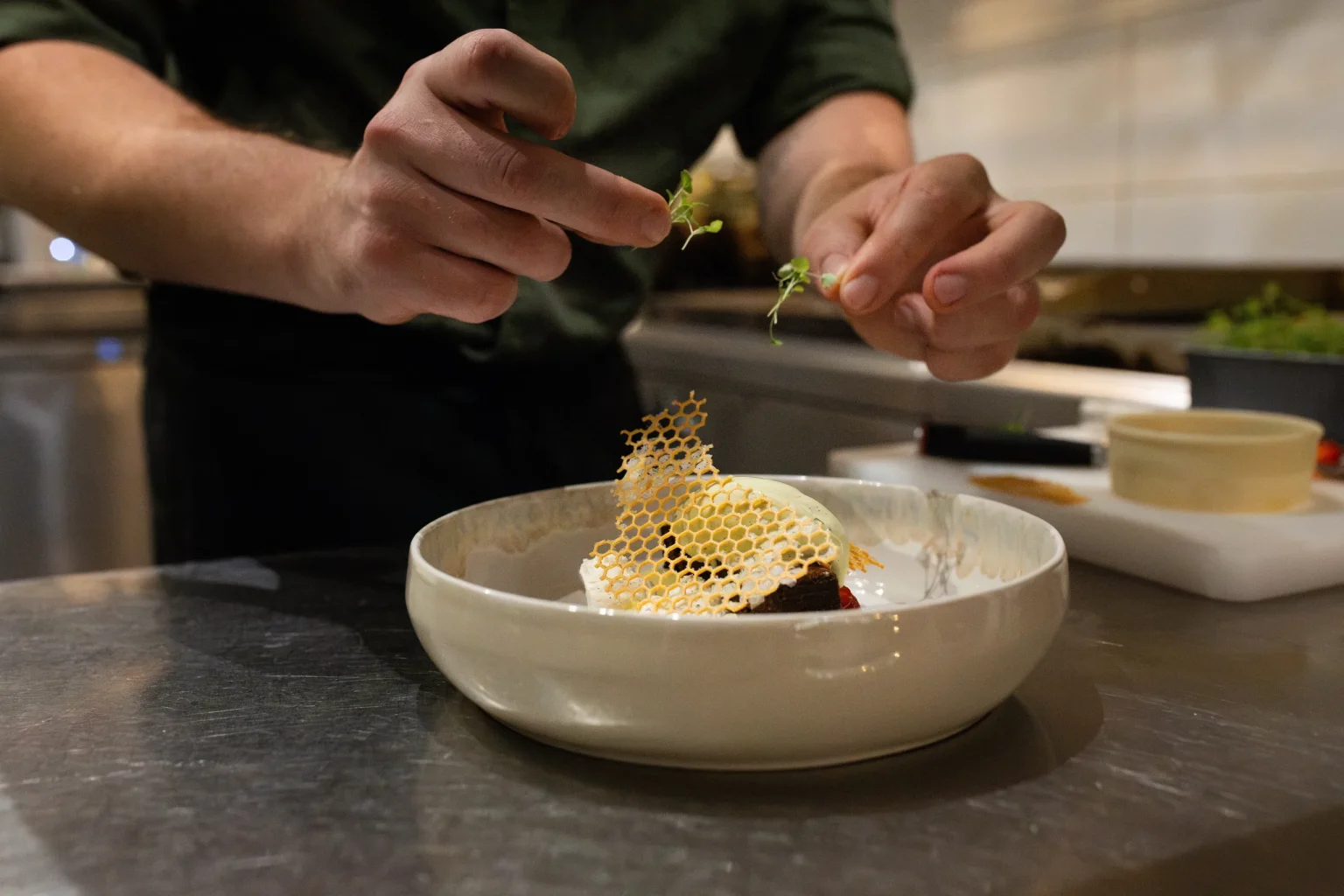 Les mains du chef déposent une pousse sur une assiette garnie d'un rayon de miel